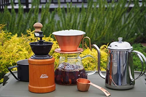 Outdoor coffee brewing setup with grinder, dripper, pot, and mug.