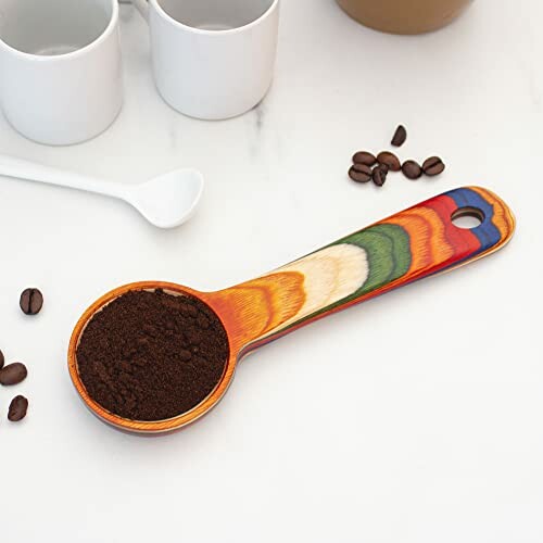 A colorful wooden coffee scoop with coffee grounds on a table, showcasing the scoop's functionality and style.