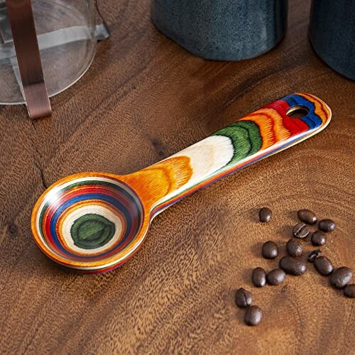 A colorful wooden coffee scoop on a wooden table with coffee beans, showcasing the scoop's functionality and versatility.