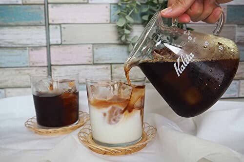 Pouring iced coffee into a glass with milk, next to another glass of cold brew.