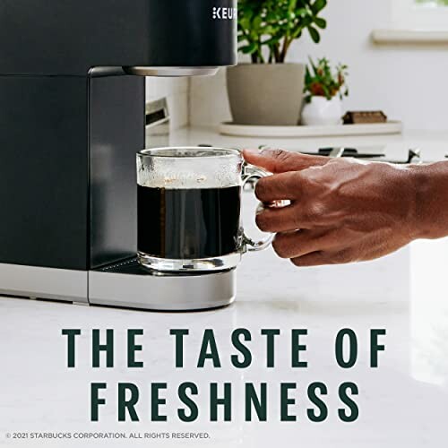 Hand holding a cup of coffee from a Keurig machine with text 'The Taste of Freshness'.