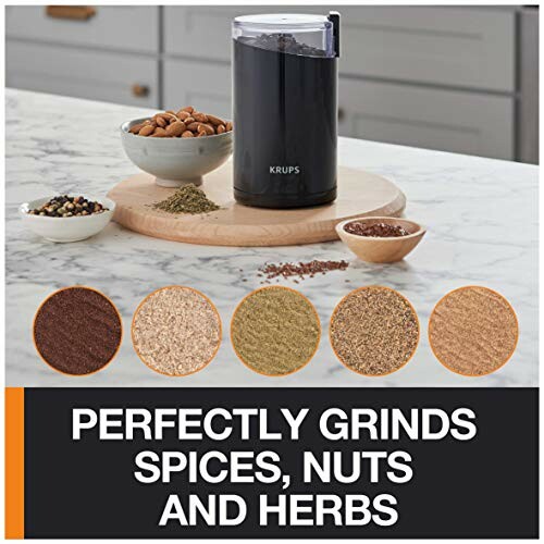 Electric grinder with spices, nuts, and herbs on a kitchen counter.